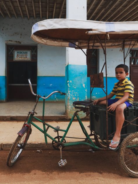 A boy sits in a Cuban rickshaw taxi